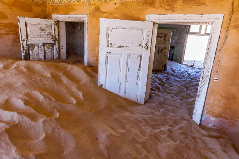 Deux portes ouvertes ensablées dans une pièce orangée abandonnée