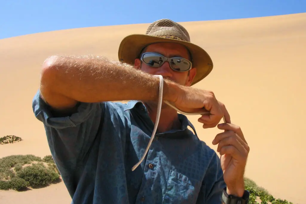 Un guide avec chapeau et lunette montre un petit serpent sur son bras