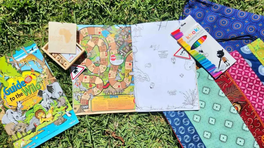 Un cahier de jeux avec crayons, cartes et sacs sont posés sur l'herbe