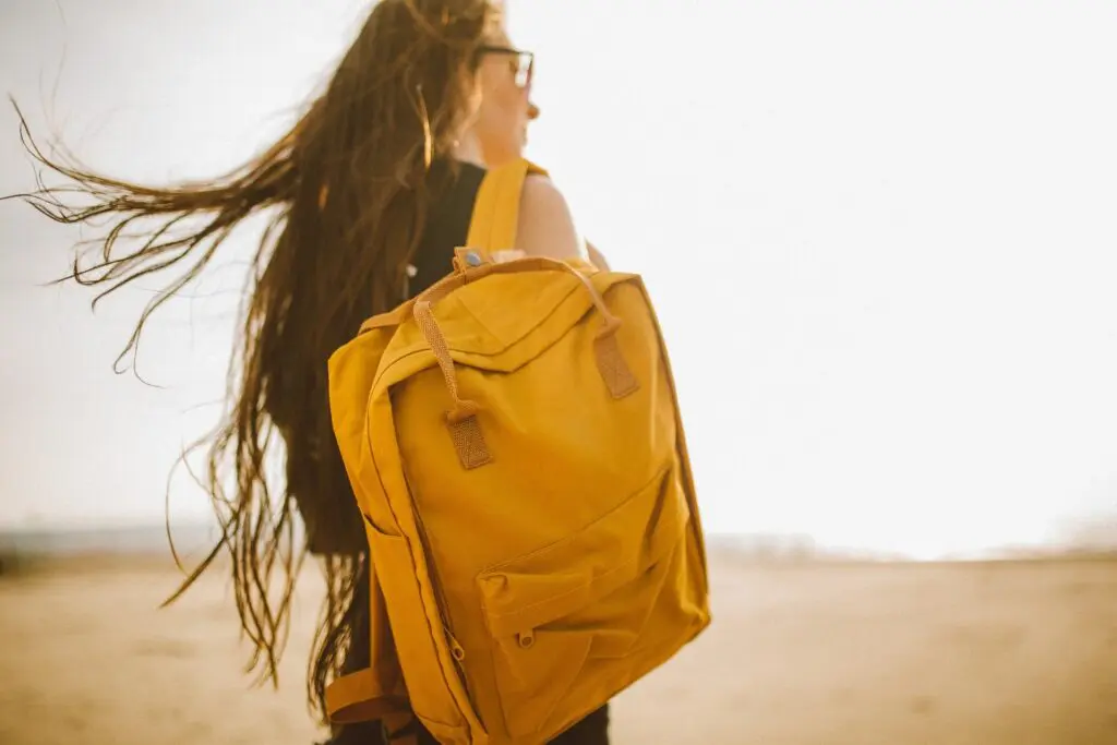 Une femme de dos, dans la nature cheveux au vent, porte un sac a dos