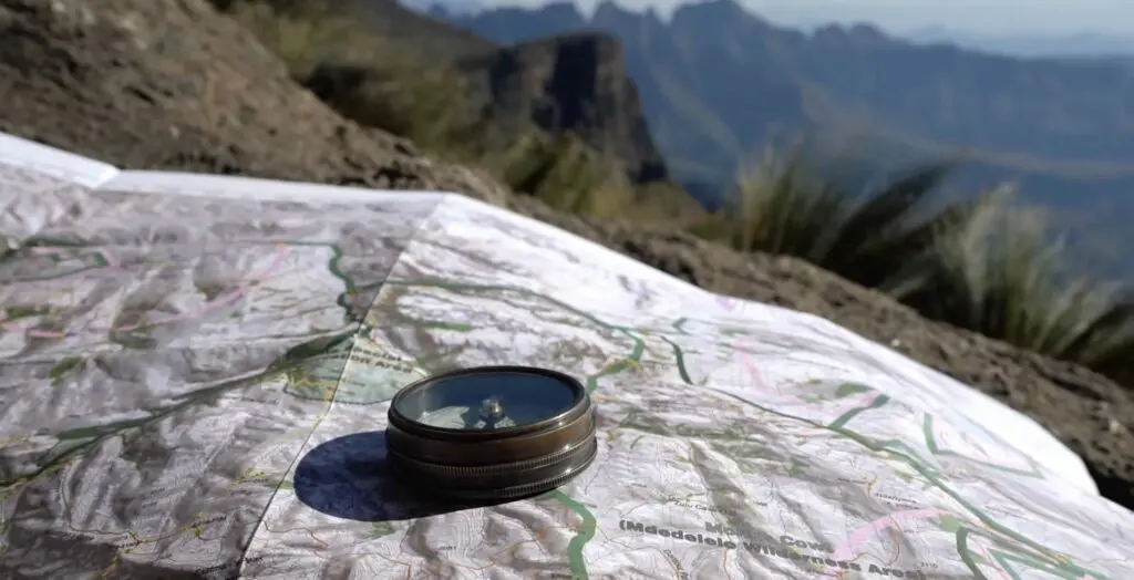 Une boussole posée sur une carte avec en toile de fond des montagnes