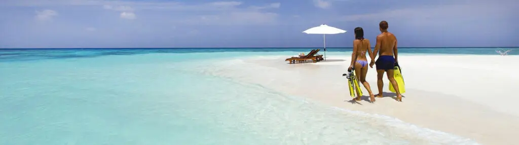 Un couple main dans la main portent des palmes jaunes sur une plage