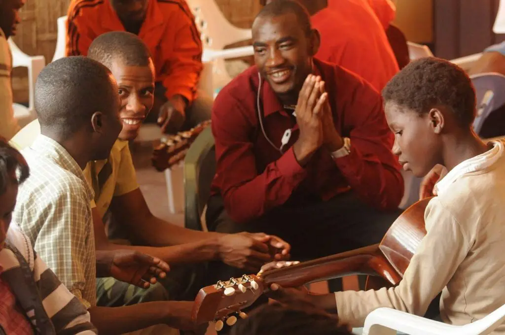 Un groupe d'hommes souriants entoure un jeune apprenant la guitare