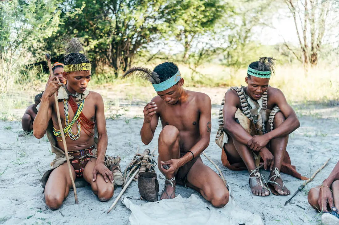 3 San assis par terre sont en train de partager leur façon de vivre