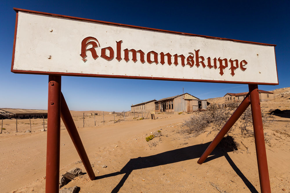 Gros plan sur le panneau de Kolmanskop avec derrière la ville ensablée