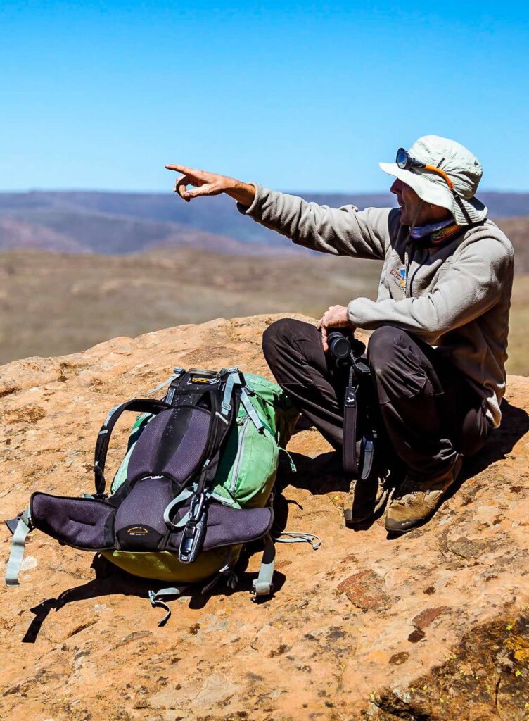 Guide montagne en pause sur un rocher et montrant une direction