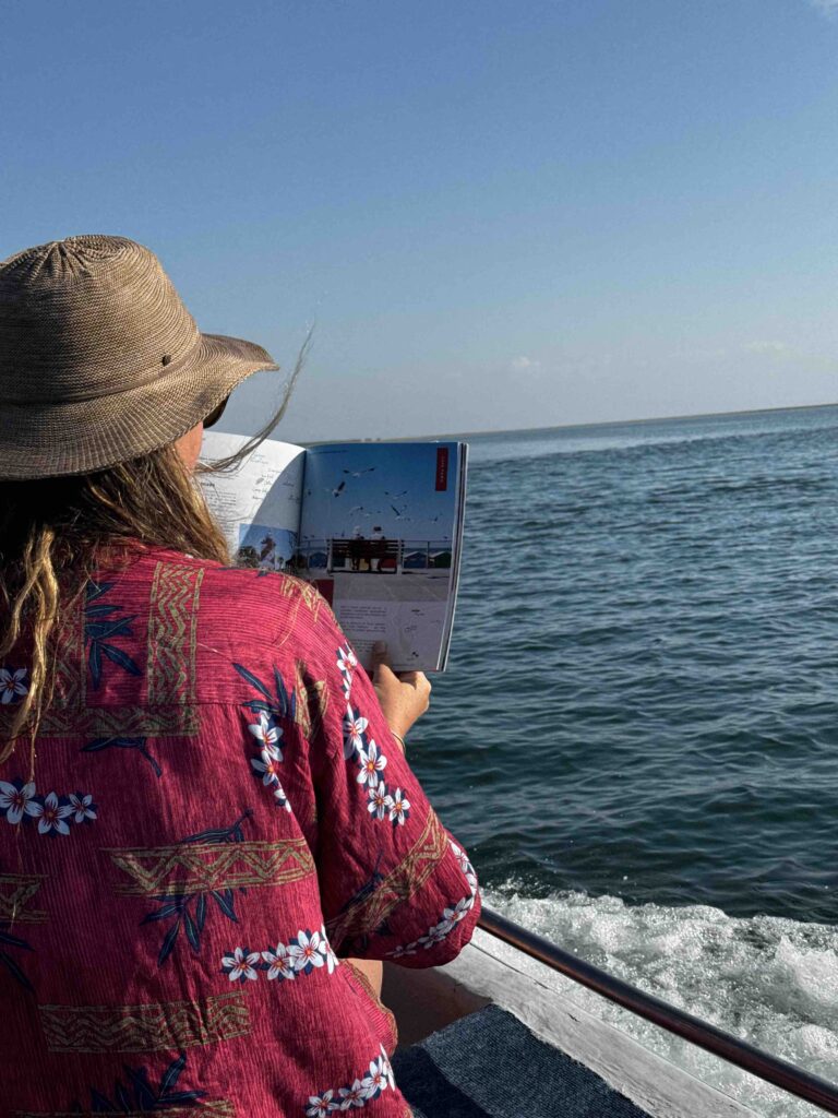 De dos, une personne dans un bateau lit le magazine Ekima Mag